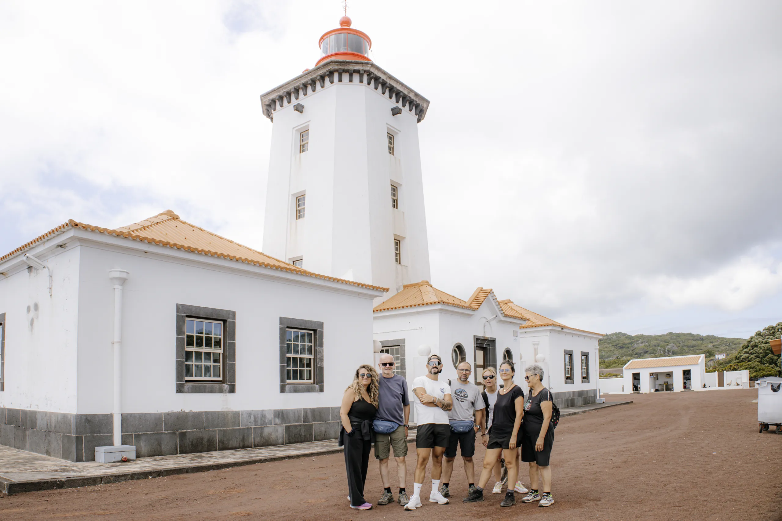 Il nostro gruppo davanti al faro bianco di Manhenha con la lanterna rossa, circondato da edifici bianchi con il tetto di tegole.