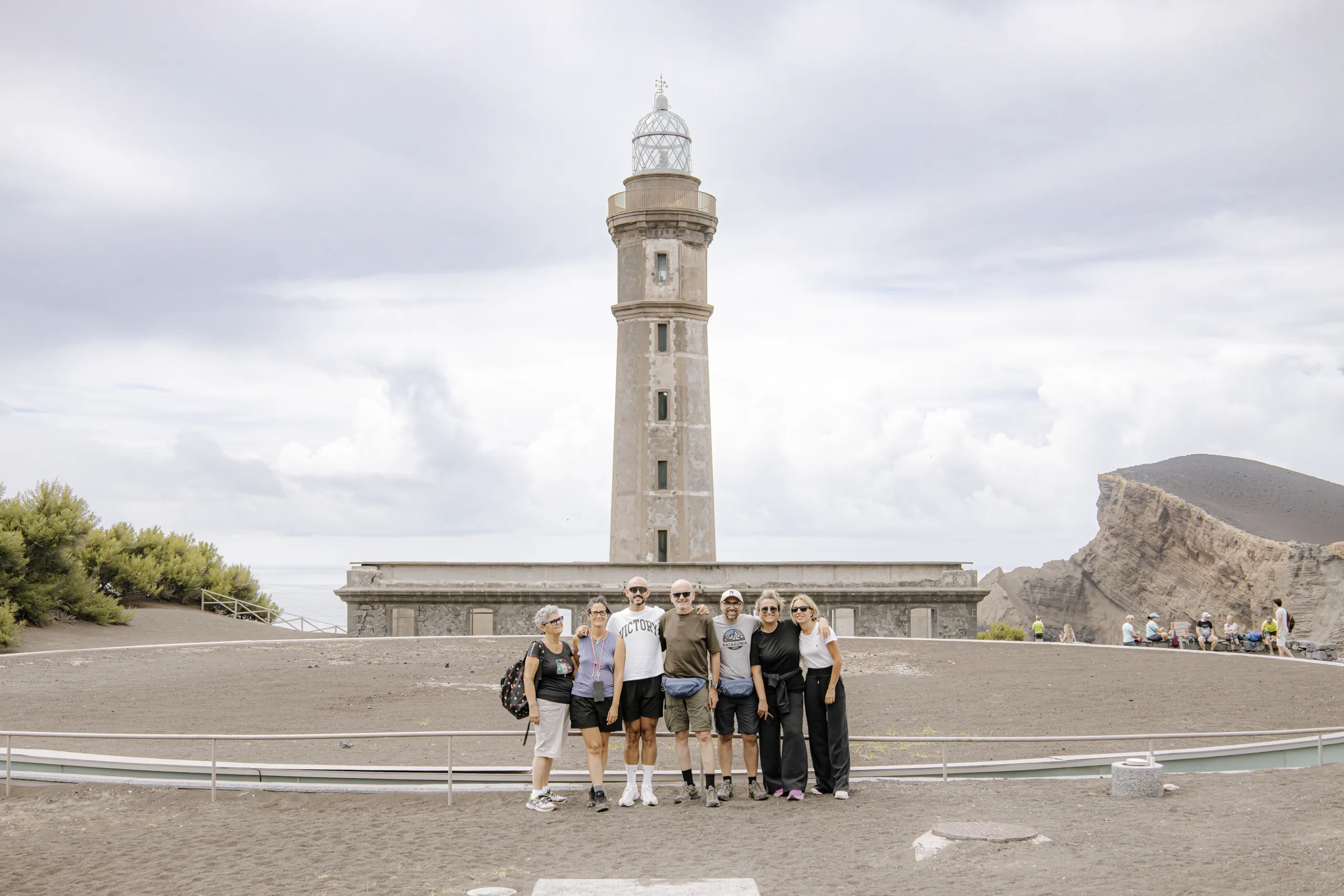 Il nostro gruppo davanti al vecchio faro in pietra di Capelinhos, semisepolto dalla cenere dell'eruzione, con le pareti del vulcano sulla destra.